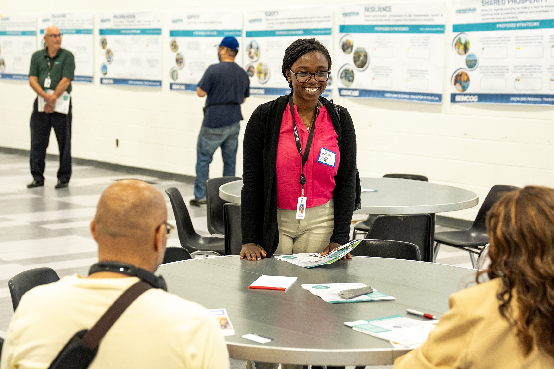 person smiling, looking at two people at table. Draft plans in the background.