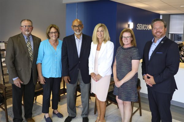 Group of seven people standing indoors in front of a SEMCOG sign, arranged in a line, wearing business or business‑casual attire in an office setting.