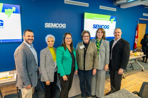 six people standing together at a SEMCOG Executive Committee in front of a SEMCOG presentation