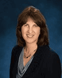 Anne Marie Graham-Hudak, Vice Chairperson at SEMCOG and Supervisor of Canton Township, smiling in a professional headshot. She is wearing a dark blazer over a gray top with a beaded necklace, posed in front of a dark blue background.