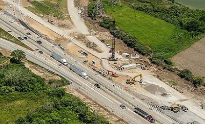 Aerial view of a highway construction zone with active machinery, vehicles, and workers alongside moving traffic