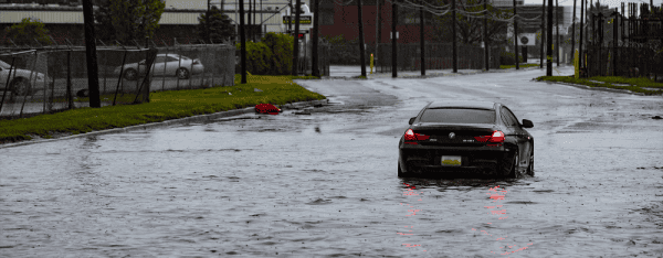 Black BMW car driving through a flooded street in Detroit, with water splashing around the tires.