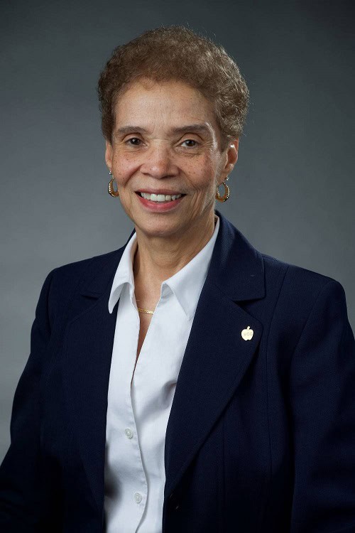 Diana McKnight-Morton, Vice Chairperson at SEMCOG and Trustee at Washtenaw Community College, smiling in a professional headshot. She is wearing a navy blazer with a white blouse and gold earrings, posed against a dark gray background.