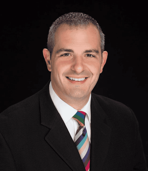 Joe LaRussa, Vice Chairperson at SEMCOG and Mayor of Farmington, smiling in a professional headshot. He is wearing a dark suit jacket, white shirt, and a colorful striped tie, posed against a black background.