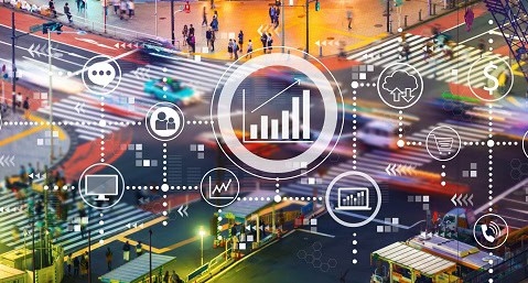 Overlay of data and technology icons on a blurred aerial view of a busy urban intersection, symbolizing smart city infrastructure and data-driven mobility solutions.