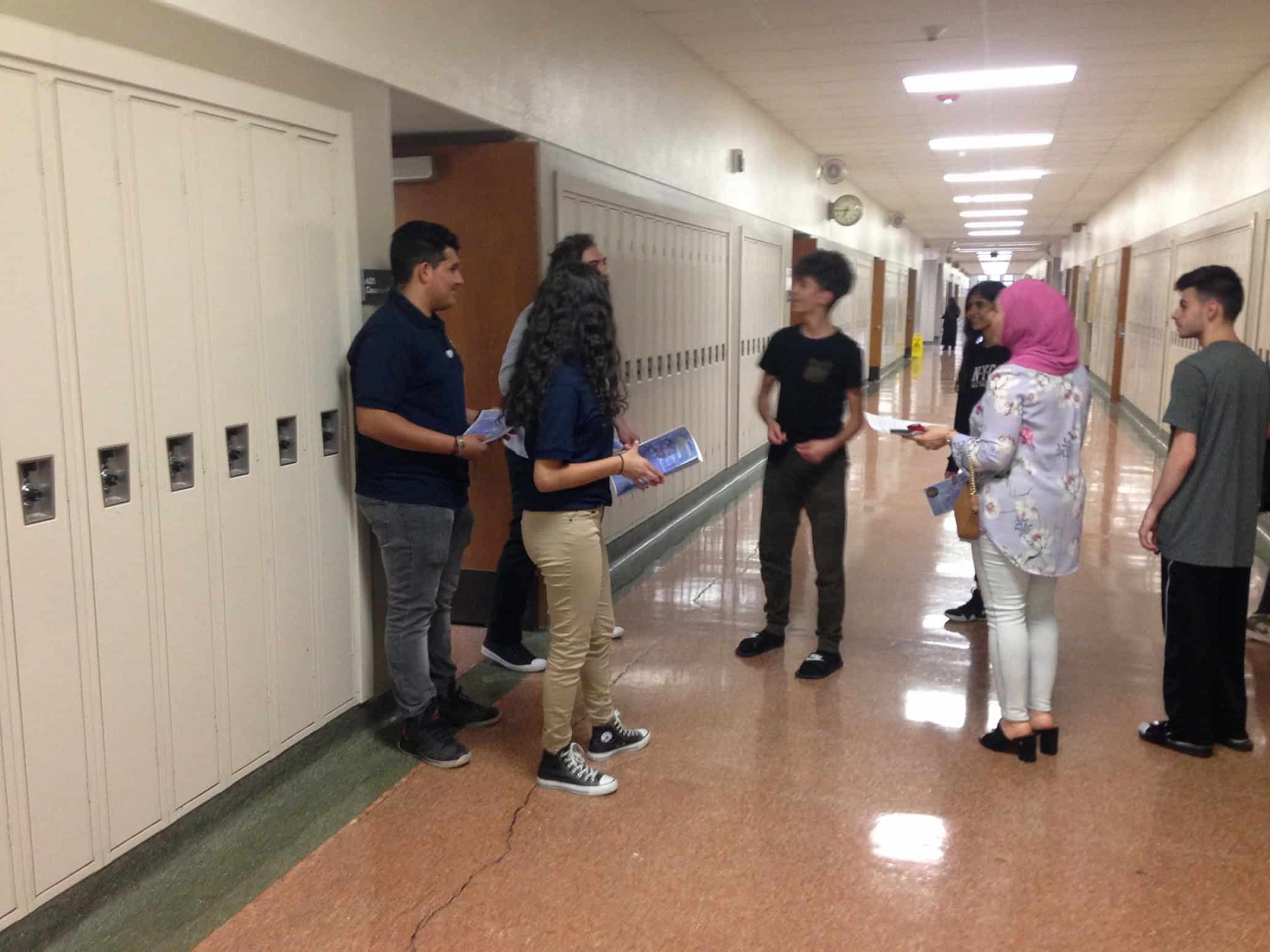 School hallway with lockers and students talking and studying.