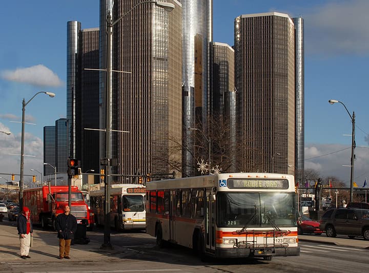 urban setting, two buses with large buildings behind them urban setting, two buses with large buildings behind them