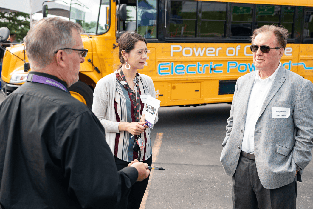 three people talking in front of an electric bus