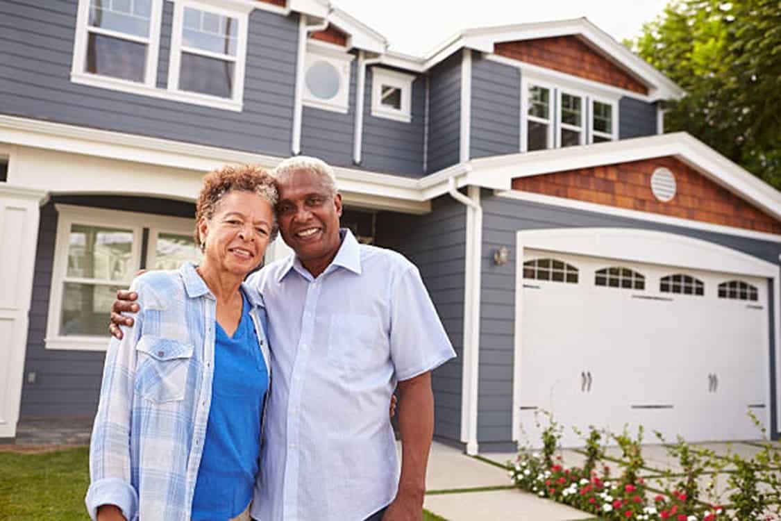 two people standing and smiling in front of a residential home