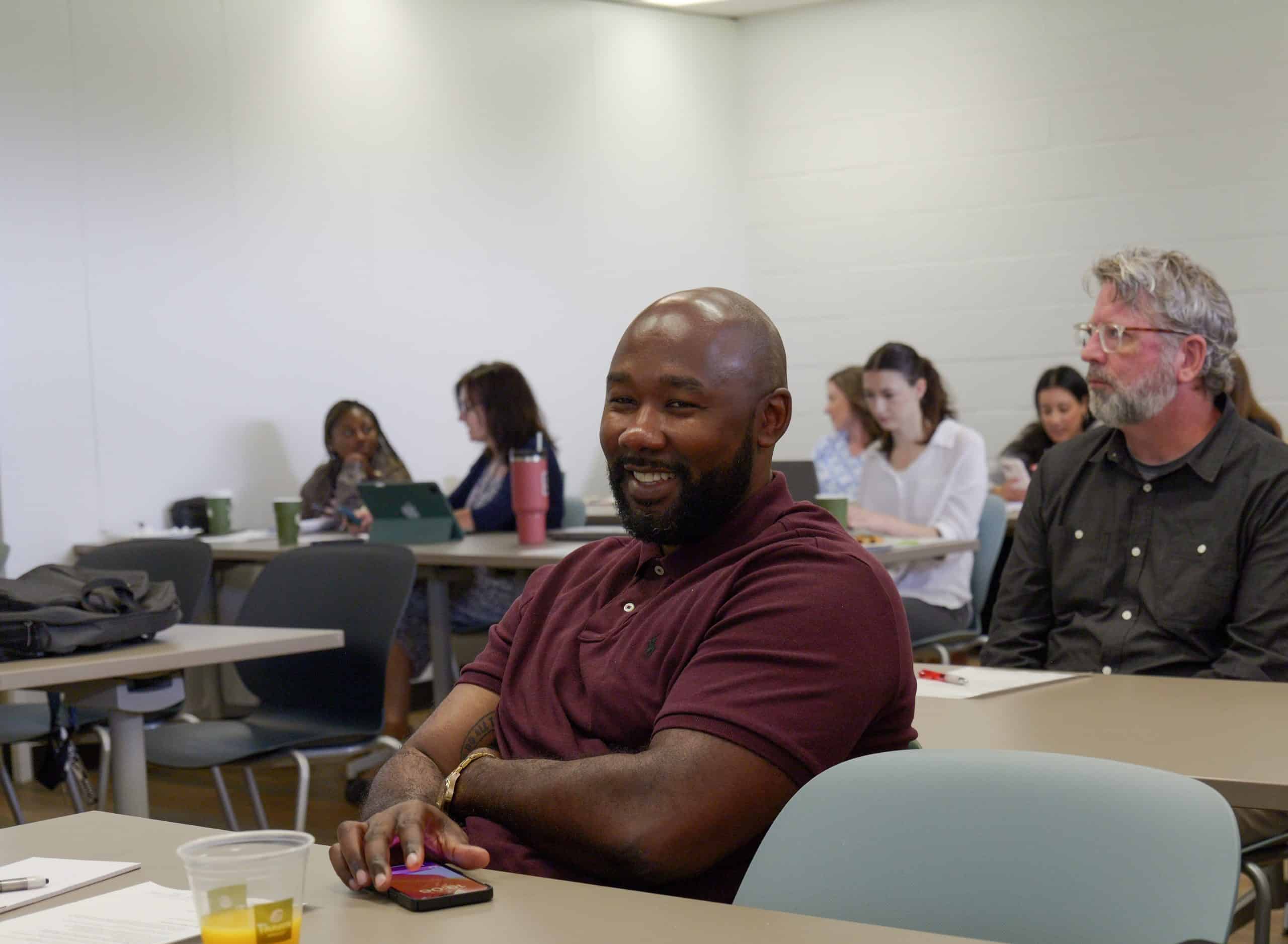 Room full of meeting attendees, focus on smiling individual