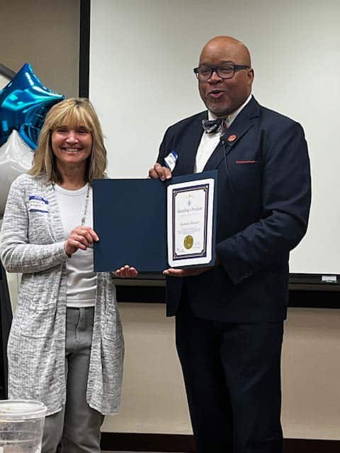 Two people standing and smiling, holding an award