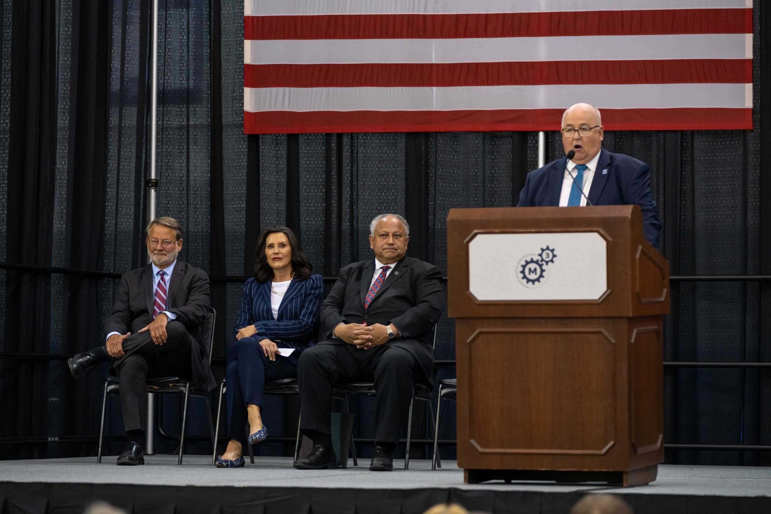 Jim Sawyer speaking at a podium with three people sitting on stage