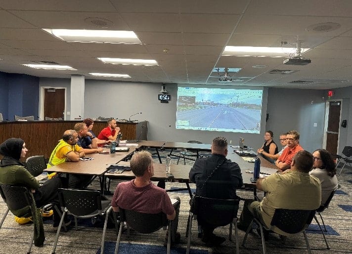 group of people sitting in a meeting with a road projected on the wall