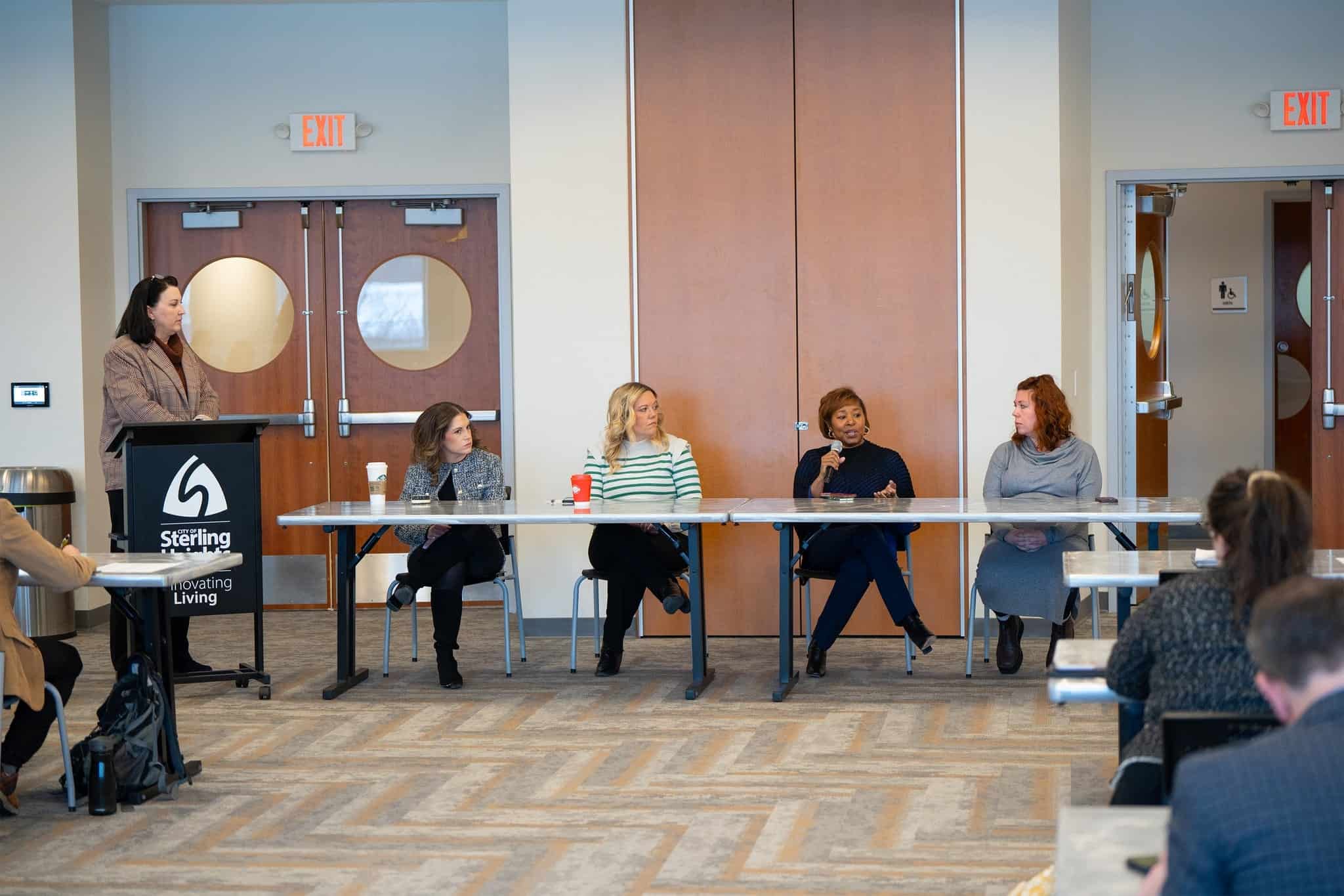 Person standing at podium next to a panel of four at a long table