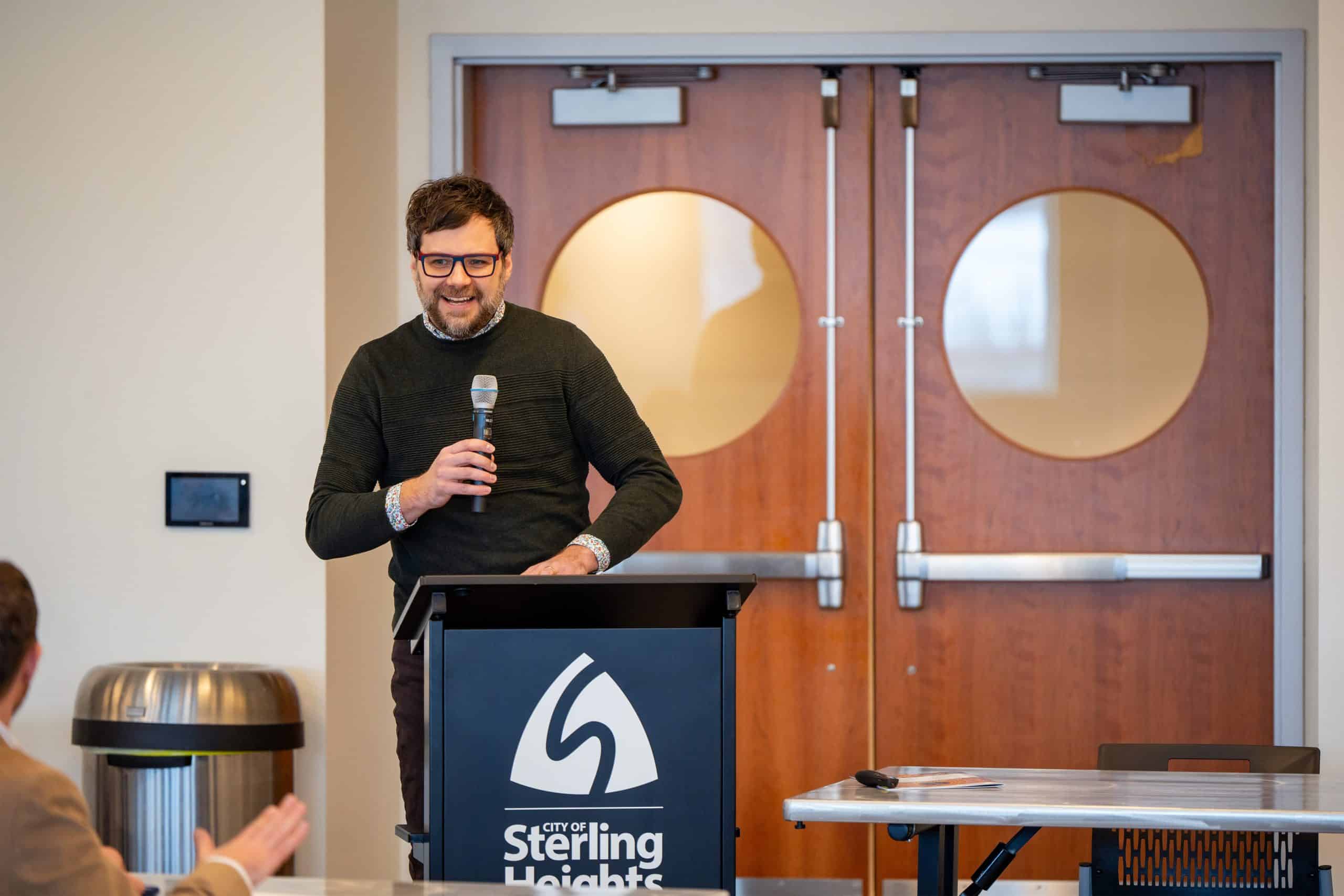 Person standing at a podium, holding a microphone and smiling