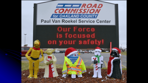 road sign that has star wars characters standing in front of road commission for oakland county, paul van roekel service center, our force is focused on your safety!