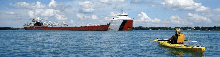 kayaker looking forwards freight ship in river
