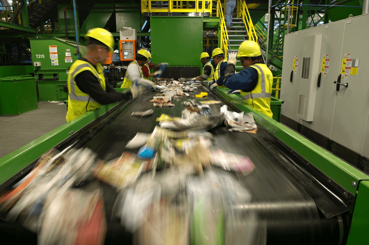 Six workers surrounding conveyor belt with materials