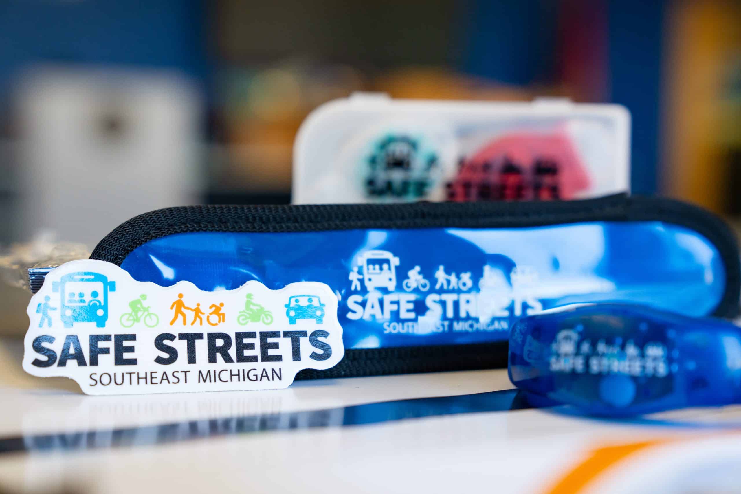 Items on a table: A 'Safe Streets' sticker, reflective armband, wristband, and bike light