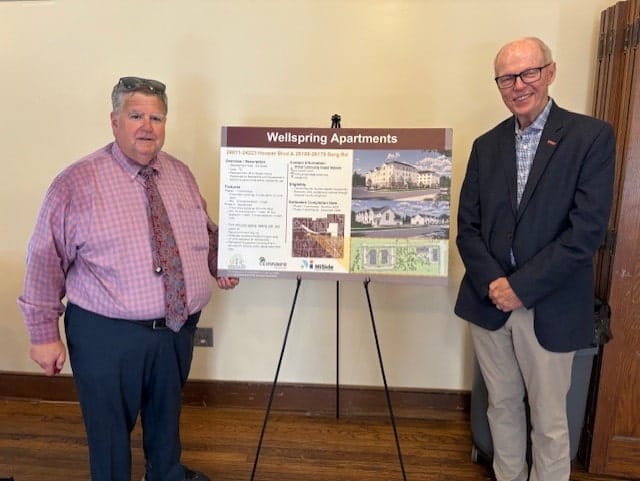 Image of Zorn and Siver in business attire standing next to a detailed project proposal for Wellspring Apartments at SEMCOG event, highlighting regional housing development.