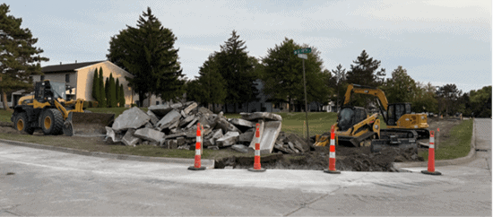 Construction site with debris, orange safety cones, and earthmoving equipment near a residential building.