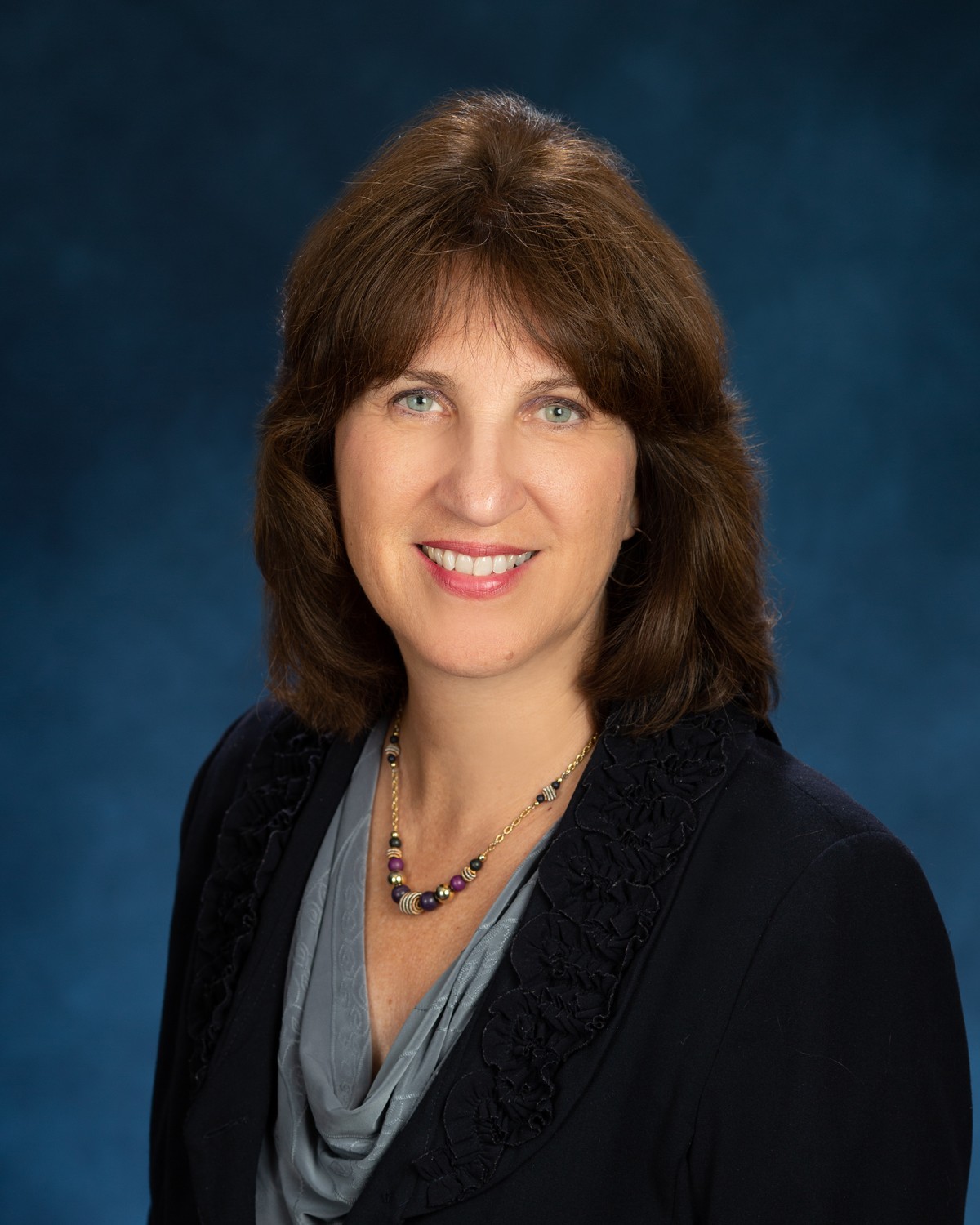 image of Anne Marie in a black blazer and grey blouse against a blue background