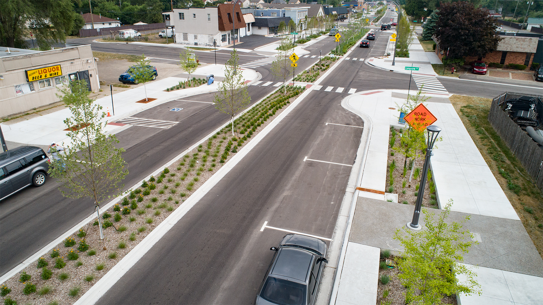 Aerial view of redesigned street with landscaped median, crosswalks, sidewalks, traffic signs, and vehicles moving through intersections.
