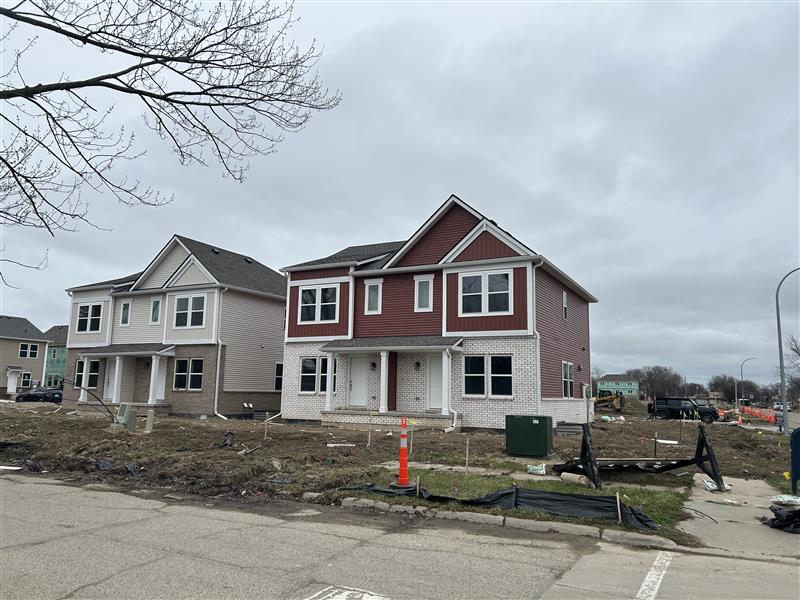 Two newly constructed duplex homes with porches and attached garages, unfinished landscaping, and construction materials visible.