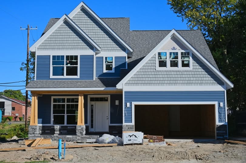 Two‑story single‑family house with blue siding, white trim, attached garage, porch columns, and unfinished yard.