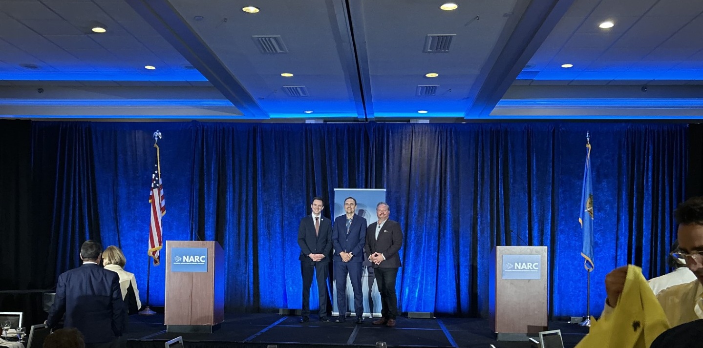 Three men standing on stage in suits and smiling