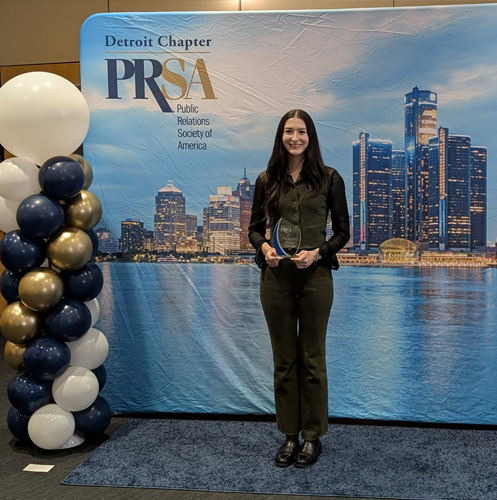 Person holding award in front of PRSA banner backdrop