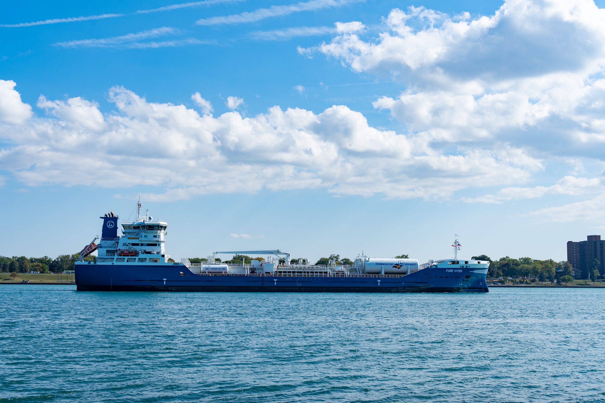 Large cargo ship sailing on water under blue sky with clouds.
