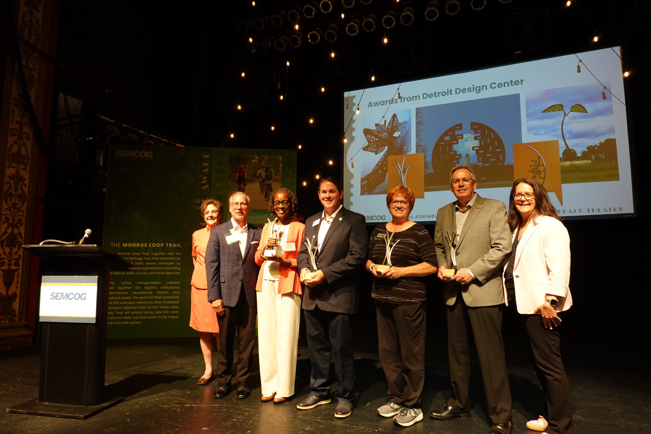 Group of award recipients standing on a stage holding trophies during a SEMCOG recognition ceremony event.