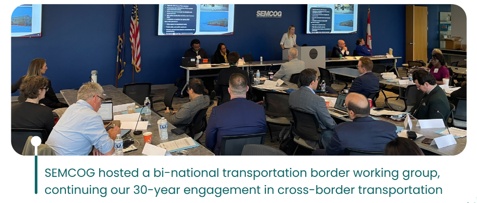 SEMCOG hosted a bilingual transportation border working group meeting. Attendees are seated around a large conference table with presentation screens displaying information.