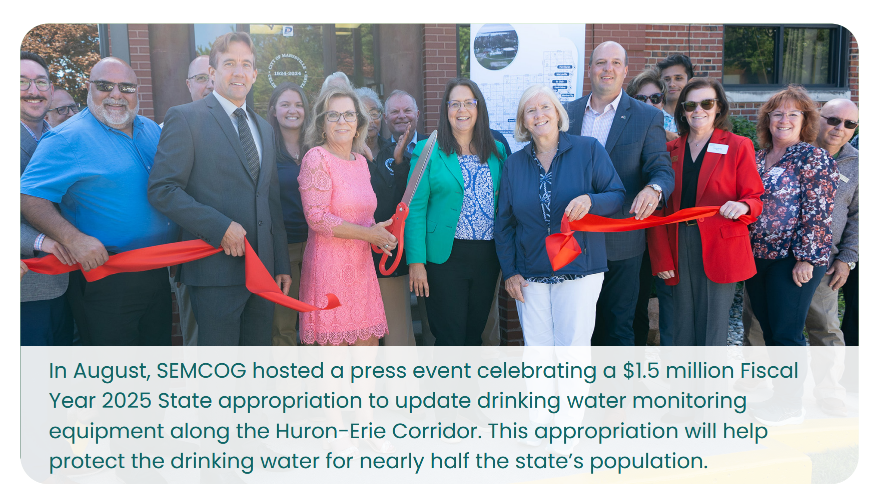 A group of people stand together at a ribbon-cutting ceremony outside a building. One individual is holding scissors, poised to cut a red ribbon. A sign in the background references a press event hosted by SEMCOG celebrating a $1.5 million state appropriation for drinking water monitoring equipment.