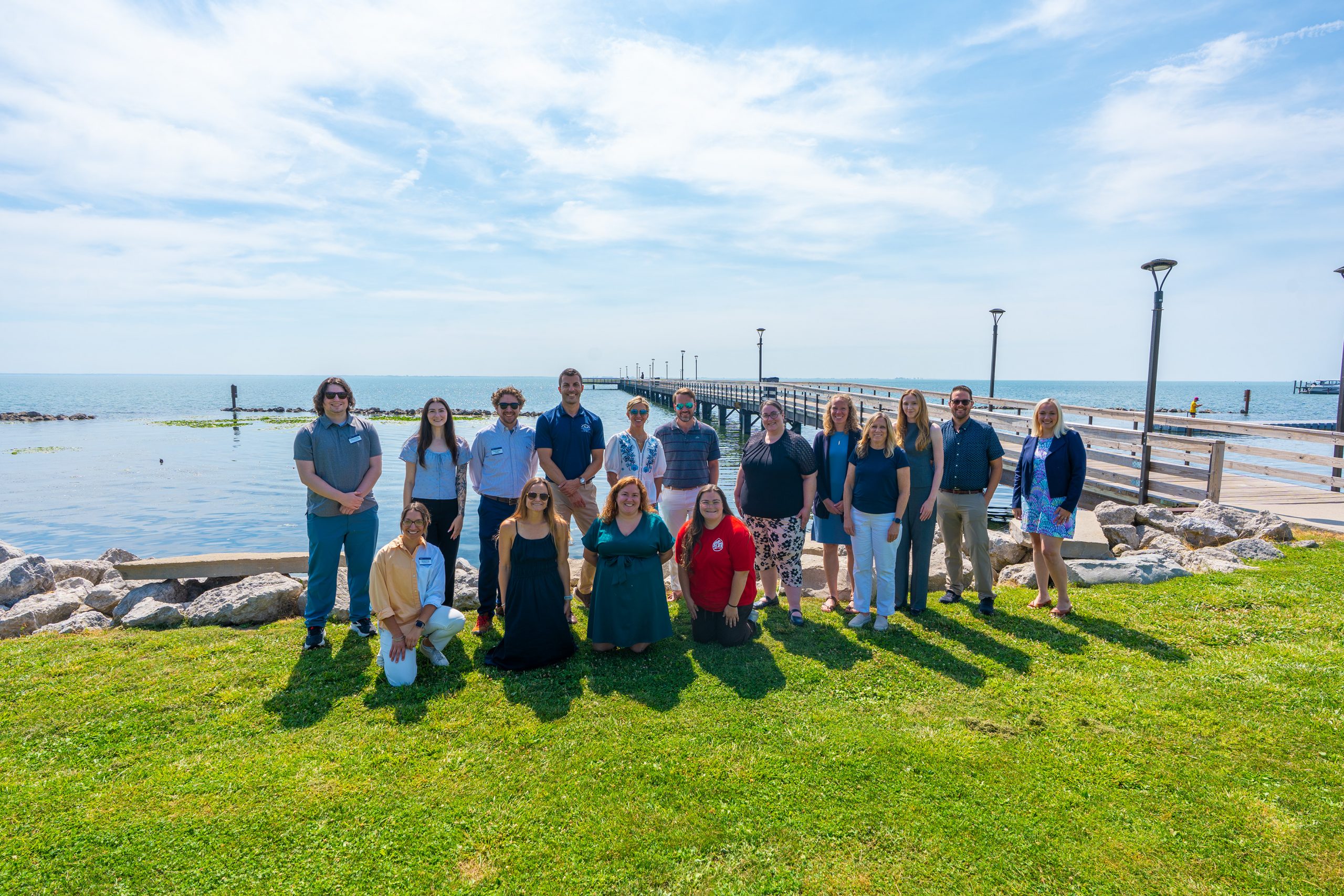 Group photo of attendees standing on a waterfront lawn beside a pier extending into the lake.