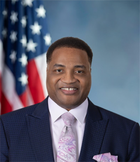 Professional portrait of a man in a suit with American flag in background.