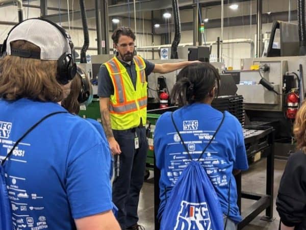 Students listen as a manufacturing professional explains equipment on a factory floor.