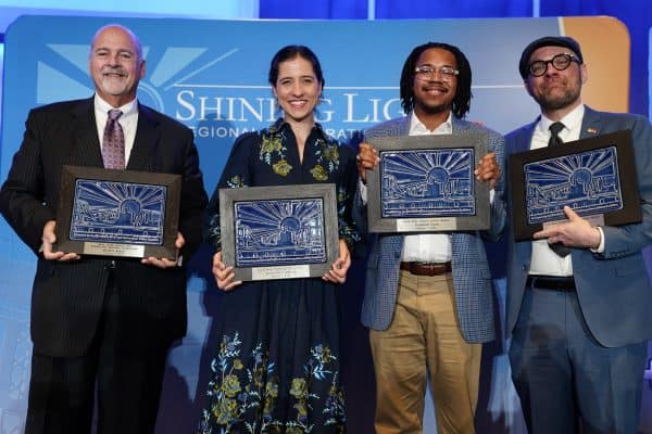 Four award recipients stand on stage holding plaques in front of a Shining Light Regional Cooperation Awards backdrop.