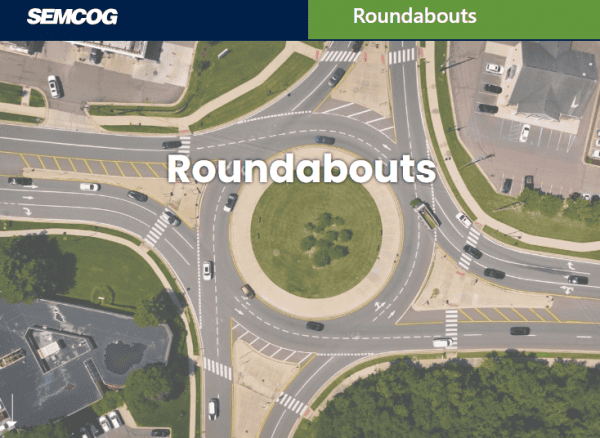 Aerial view of a multi-lane roundabout with vehicles traveling through surrounding roads and a landscaped center island.
